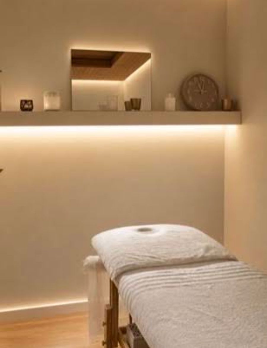 Calm treatment room with warm lit shelf and white linen massage bed at Enyo Thai Massage Athens